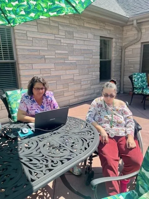 Two women sitting outside at a table with one of them on a laptop